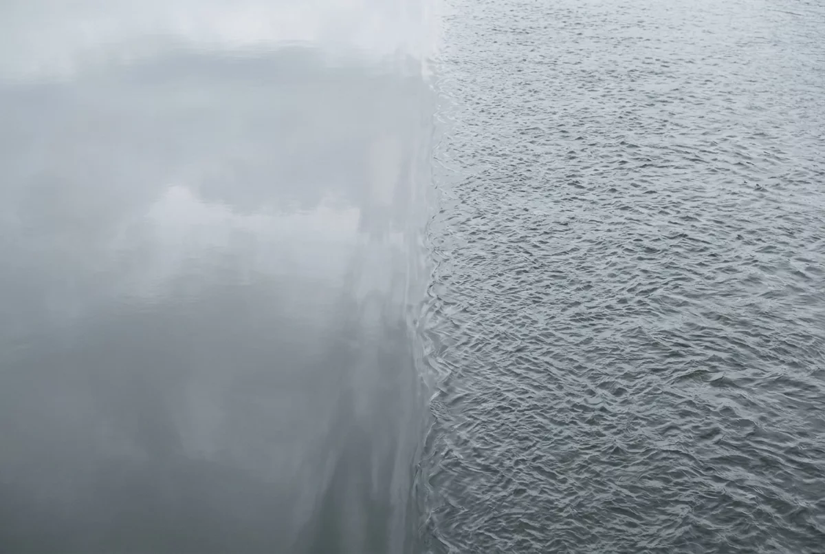 Wasseroberflaeche halb spiegelglatt halb von Wellen bewegt